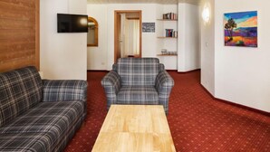 A room with a wooden ceiling, a red carpet, a wooden coffee table, two plaid sofas, a television, a bookshelf, and a painting. - Chalet Abendrot apARTments by Interhome (Grindelwald)