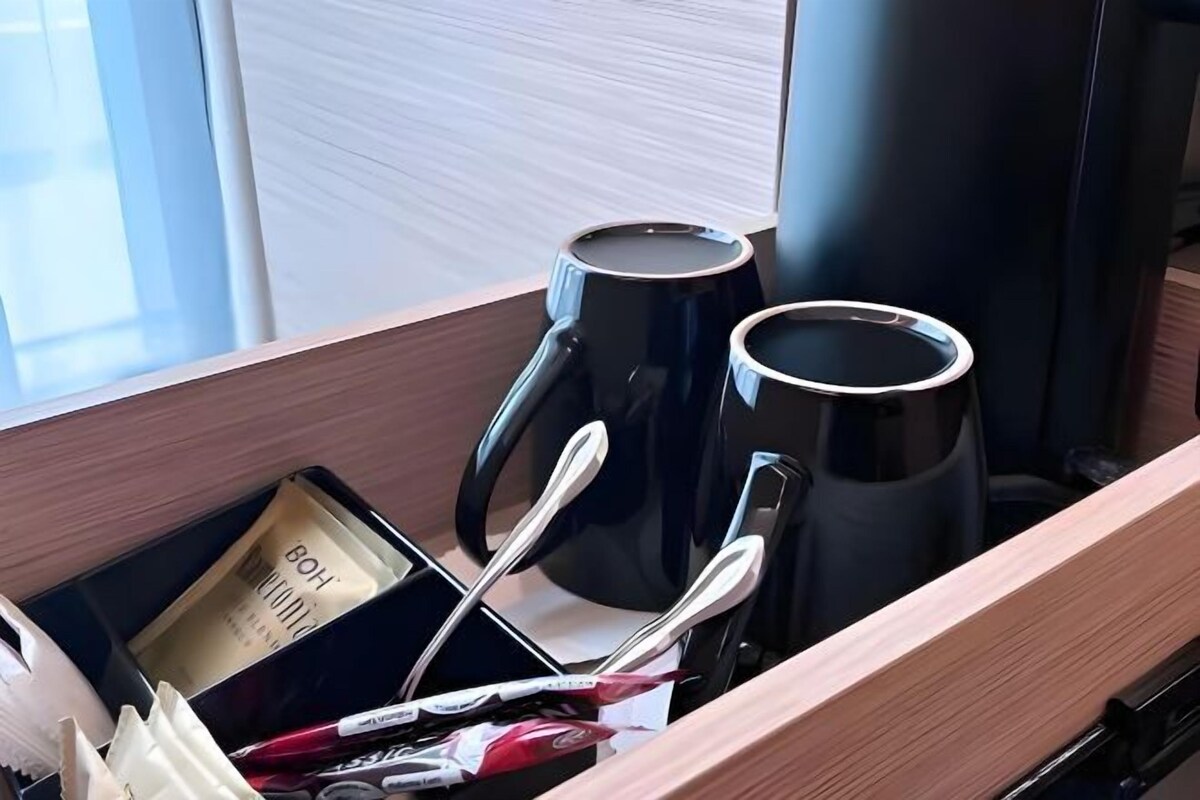 Un cajón con una cafetera negra, dos tazas negras, una caja de pañuelos y un par de tijeras.