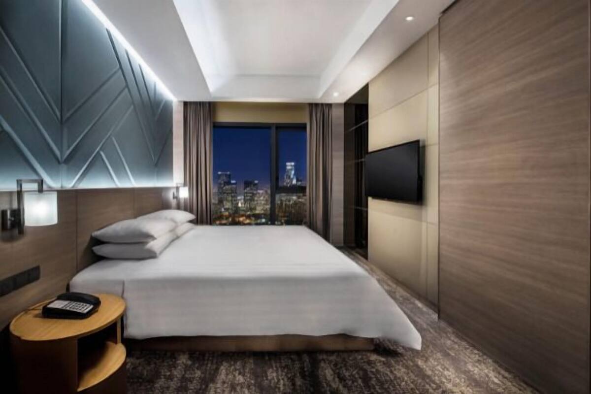 Una habitación de hotel moderna con una cama grande, vistas a la ciudad, un televisor de pantalla plana y una mesita auxiliar.