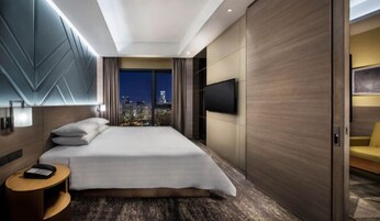 A modern hotel room with a large bed, a city view, a flat-screen TV, and a small side table.
