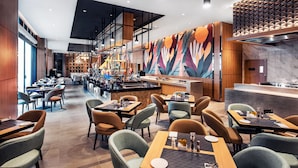 Un restaurante moderno con barra central, varias zonas de estar y un mural llamativo en la pared.