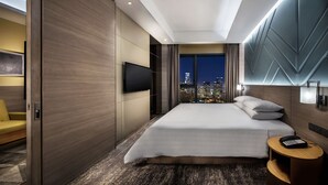 Habitación de hotel moderna con una cama grande, un televisor montado en la pared, vista a la ciudad y una mesita de noche con teléfono.