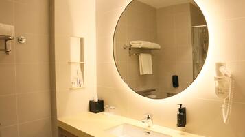 A bathroom with a round mirror, a sink, a towel rack, a phone, and a soap dispenser.