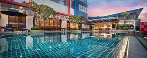 A modern hotel pool area with a clear blue pool, outdoor seating, and a view of the ocean at sunset. - Sunway Hotel Big Box (Iskandar Puteri)