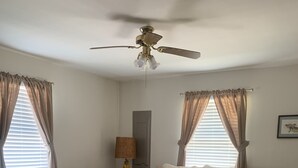 A bedroom with a bed, a ceiling fan, a nightstand with a lamp, and a window with curtains. - Cottage on the Bay (Fishing Creek)
