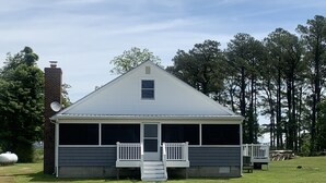 A single-story building with a gabled roof, a front porch with white railings, and a small window above the door. - Cottage on the Bay (Fishing Creek)