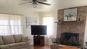 A living room with a sofa, TV, fireplace, and a ceiling fan. - Cottage on the Bay (Fishing Creek)