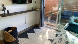 A modern bedroom with a flat-screen TV, a bed with a patterned duvet, a woven basket, and a sliding glass door leading to an outdoor area.