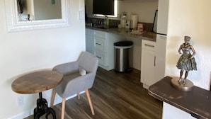 A compact kitchen with a sink, stove, and a small trash bin. There is a dining area with a table and a chair.