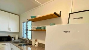 A modern kitchen with white cabinets, a granite countertop, a Whirlpool refrigerator, and a wooden shelf above the sink.