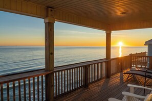 A wooden deck with a railing overlooking the ocean at sunset.