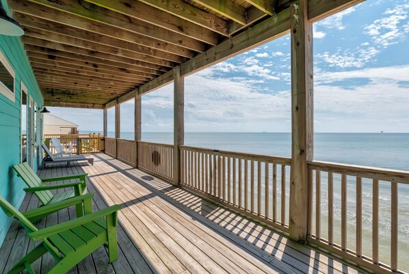 A wooden deck with a railing, green chairs, and a view of the ocean.