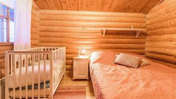 A cozy log cabin bedroom with a crib, a bedside table with a lamp, and a bed with a patterned blanket.