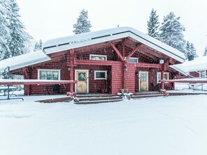 Eine rote Holzhütte mit einem schneebedeckten Dach, umgeben von schneebedeckten Bäumen.