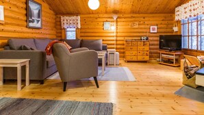 L’intérieur d’une cabane en rondins, avec un canapé, un fauteuil, une commode en bois, un téléviseur et une cheminée.