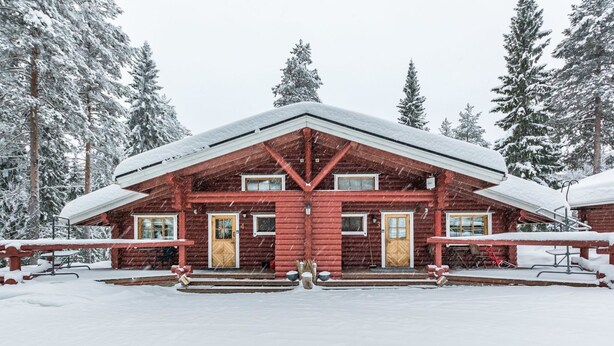 Une cabane en rondins à la façade symétrique, dotée d’une entrée centrale et d’un porche abrité.