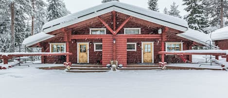 Eine Blockhütte mit steilem Dach, mehreren Fenstern und einer Veranda mit Stufen zum Eingang.