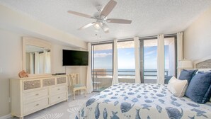 Ein Schlafzimmer mit Bett, Kommode, Fernseher und Meerblick.