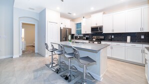 A modern kitchen with white cabinets, stainless steel appliances, and a central island with bar stools. - AS2811  Storey Lake Condo 5 bed 5 bath  Free Waterpark (Kissimmee)