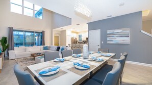 A modern living room with a dining area, large windows, and a kitchen in the background. - AS2811  Storey Lake Condo 5 bed 5 bath  Free Waterpark (Kissimmee)