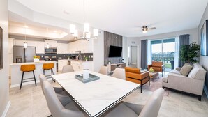 A modern kitchen with a central island, a dining area with a marble table, and a living room with a sofa and TV. - JC108 Storey Lake, 3Bed&2Bath Free Waterpark (Kissimmee)