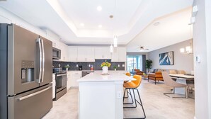 A modern kitchen with stainless steel appliances, a central island, and a dining area with contemporary chairs. - JC108 Storey Lake, 3Bed&2Bath Free Waterpark (Kissimmee)