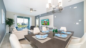 A modern dining area with a large table set for six, white chairs, and a television mounted on the wall.