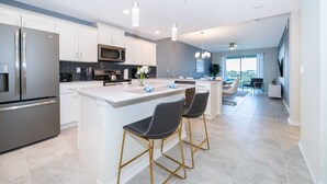 A modern kitchen with white cabinetry, stainless steel appliances, and a central island with bar stools.