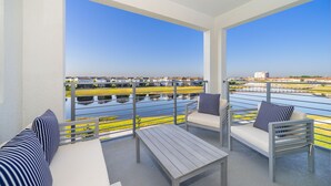 Un balcon avec vue sur un plan d’eau et des bâtiments. On y trouve deux canapés et une table.