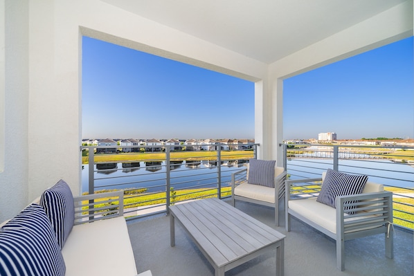 A balcony with a view of a water body and buildings. There are two sofas and a table.