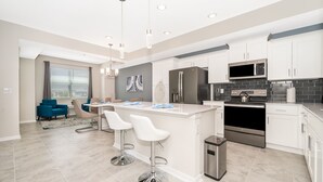 Una cocina moderna con armarios blancos, electrodomésticos de acero inoxidable y una isla central con taburetes de bar.