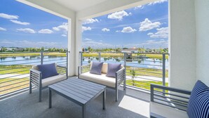 Un balcón con vistas a un lago y un edificio lejano. Hay dos sofás con almohadones a rayas y una mesita.