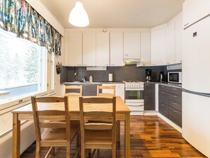 Eine moderne Küche mit weißen Schränken, einem Holztisch und einem großen Fenster.