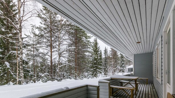 A covered wooden deck with benches, surrounded by snow-covered trees.