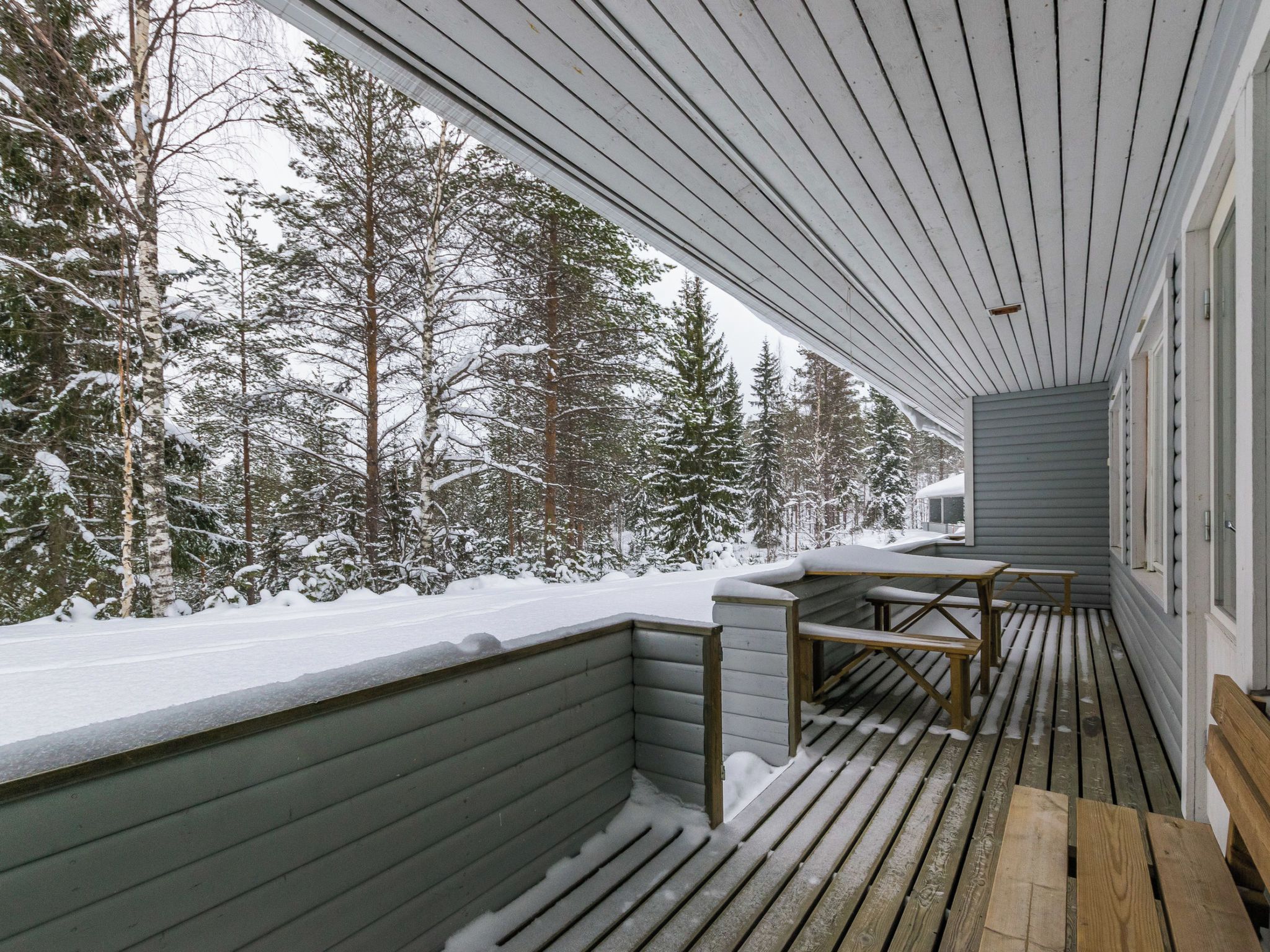 A covered outdoor area with a bench and a table, surrounded by snow-covered trees.