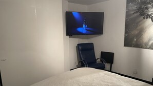 A bedroom with a bed, a blue chair, a television mounted on the wall, and a painting of a tree. - Steps from Gondola, views of Beaver Creek slopes, newly remodeled 2 BR 2BA Condo (Avon)