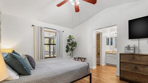 A bedroom with a bed, wooden floor, a ceiling fan, a TV, and a plant. - Stylish Pool Home w/ Grill by GNV's Best Dining! (Gainesville)