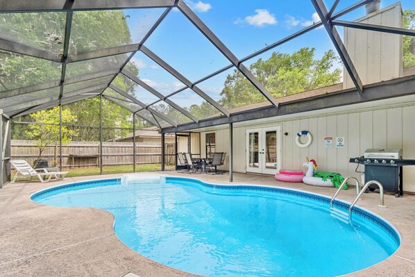Une piscine couverte avec un espace patio, un barbecue et une cour arrière clôturée.