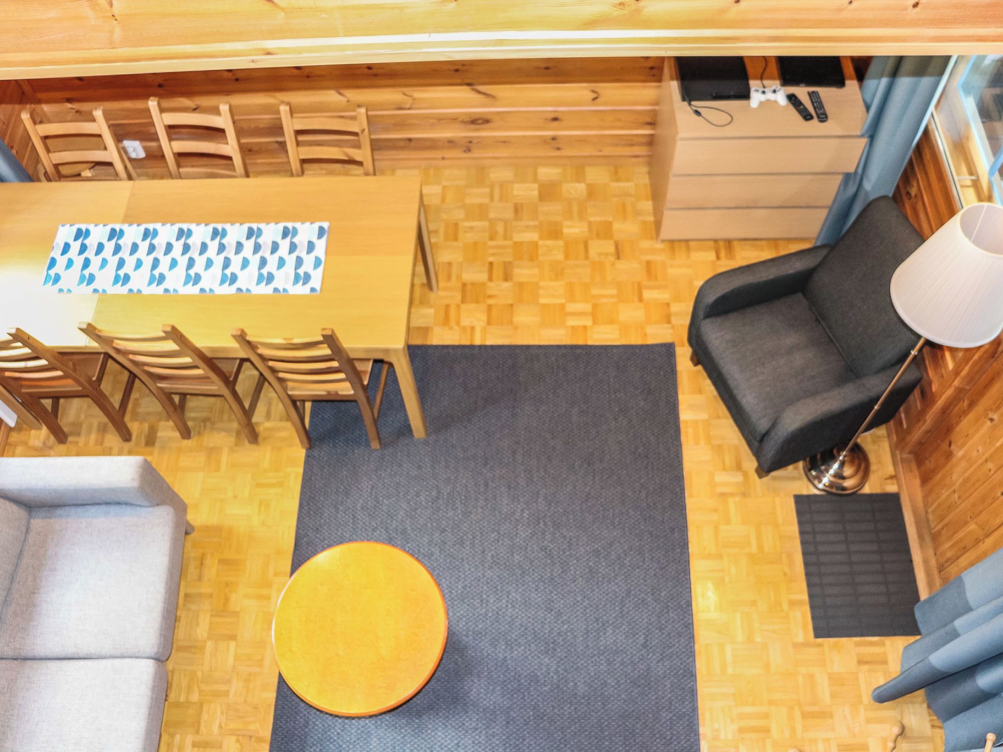 A compact room with a wooden dining table, chairs, a sofa, a small round table, and a lamp.