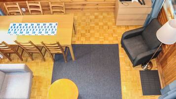 A compact room with a wooden dining table, chairs, a sofa, a small round table, and a lamp.