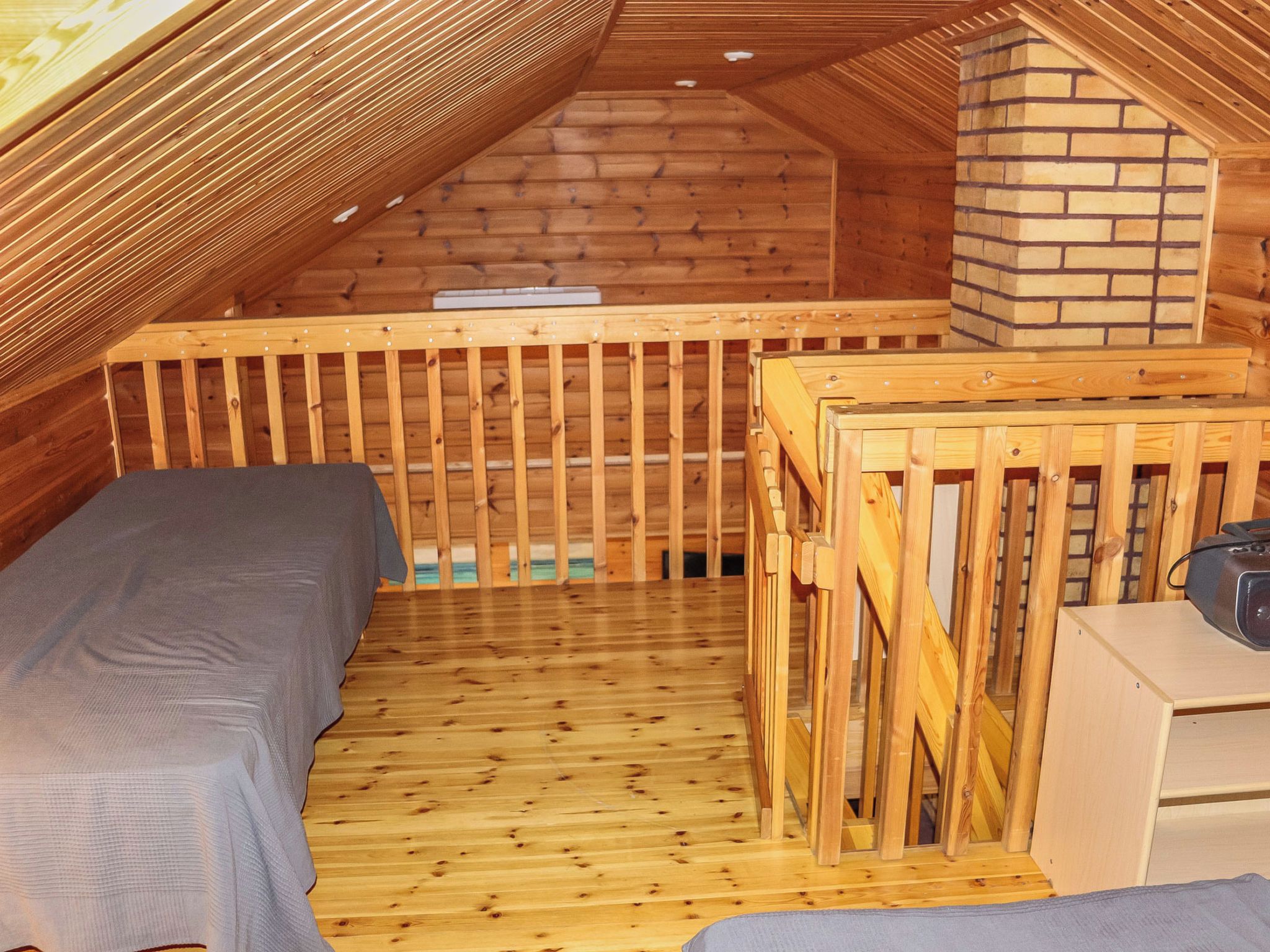 A small, wooden attic bedroom with a bunk bed, a wooden crib, and a fireplace.
