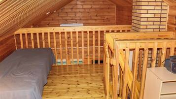A small, wooden attic bedroom with a bunk bed, a wooden crib, and a fireplace.