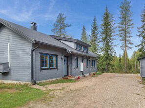 A two-story house with a gravel driveway and a forested backdrop.