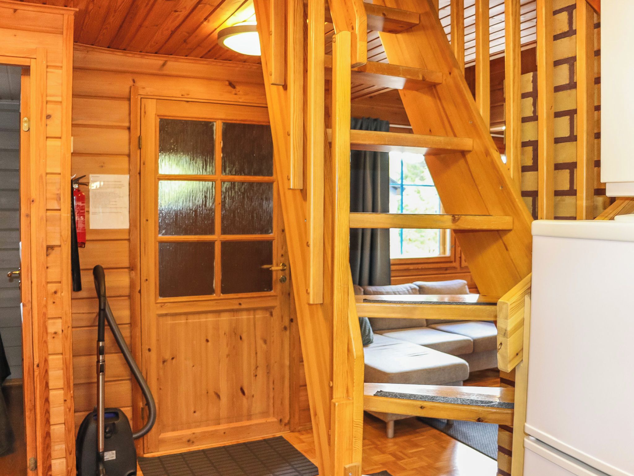 Un interior de madera con una escalera, una puerta con paneles de vidrio esmerilado y una zona de estar con cojines.
