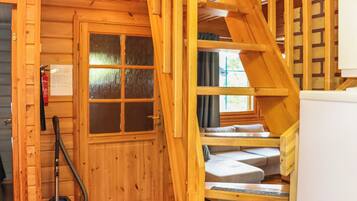Un interior de madera con una escalera, una puerta con paneles de vidrio esmerilado y una zona de estar con cojines.