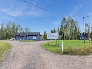 A gravel driveway leading to a blue building with a sign indicating 'Paljakan Loma-Asunot' and 'Loma-Asunot Tontjeja'.