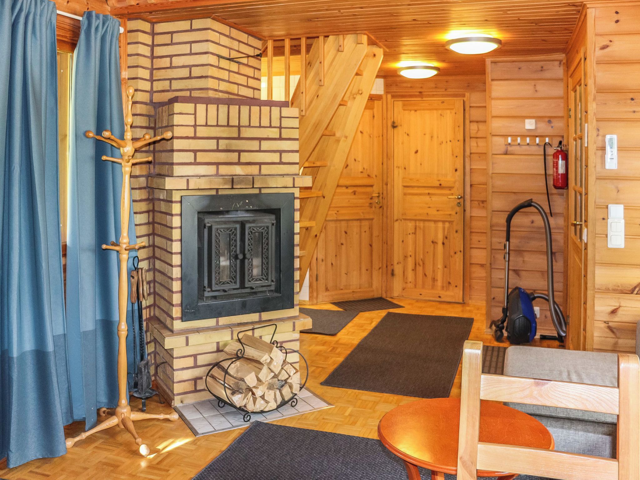 A log cabin interior with a fireplace, wooden walls, a staircase, and a vacuum cleaner.