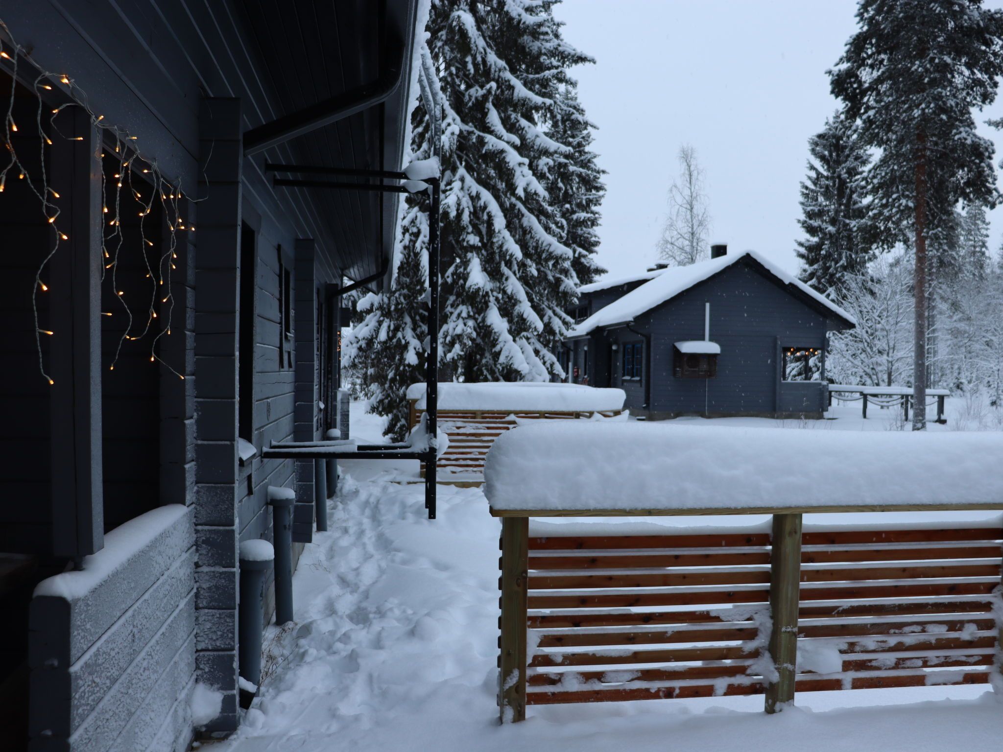 A snow-covered outdoor area with a wooden bench and a building with a dark facade.