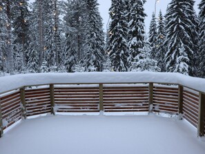 A snow-covered wooden bench with a view of snow-laden trees in the background.
