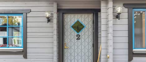 Una casa con el número 2 en la puerta, una ventana con marco azul y una escoba apoyada en la pared.